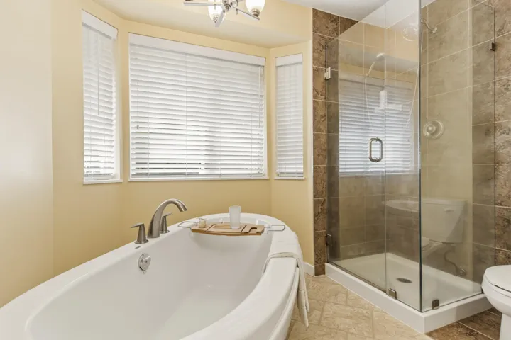 Soaking tub with brushed nickel fixtures, surrounded by bay windows with white blinds