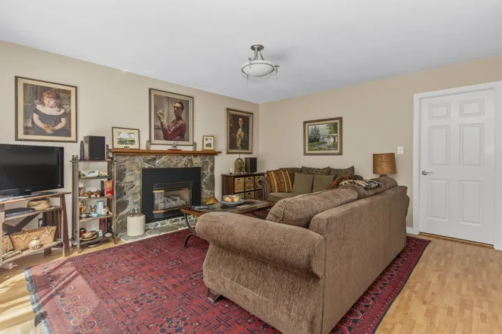 Living area featuring a stone-clad fireplace with a hearth, wood-finish flooring, and light neutral wall paint