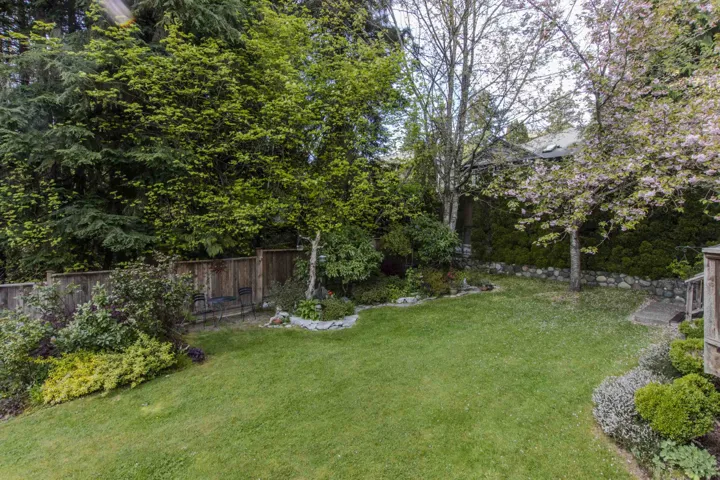 Expansive backyard featuring a lush lawn, mature trees, and layered landscaping with varied foliage