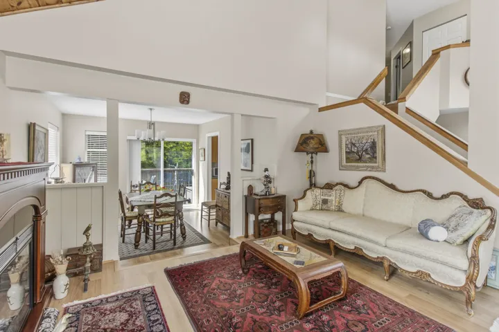 Living area with light-toned wood-finish flooring, a prominent staircase with wood railings, and a fireplace with a wood mantle