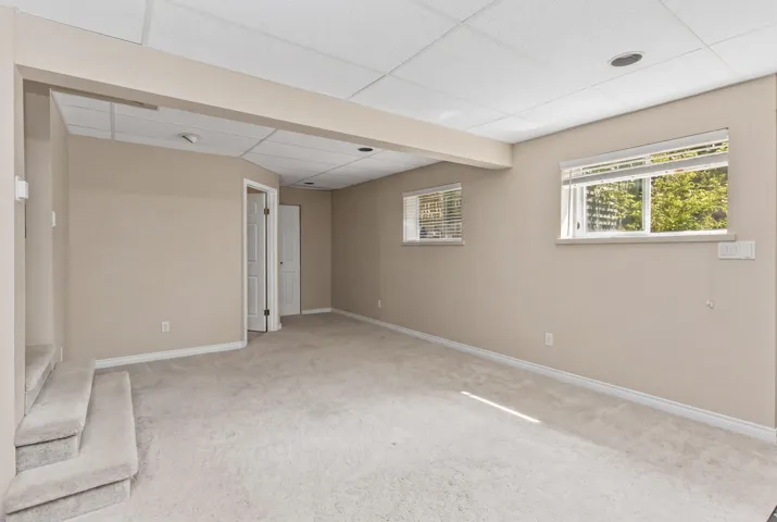 Carpeted lower-level room featuring neutral wall paint, two windows with blinds, a drop ceiling, and recessed lighting