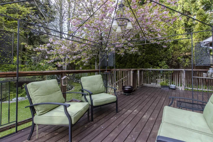 Spacious outdoor deck featuring wood flooring, a decorative metal pergola, and a built-in hanging light fixture