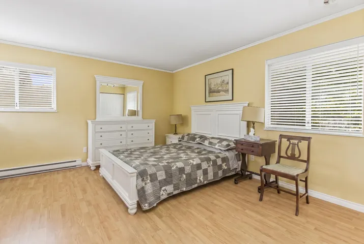 Bedroom featuring wood-finish flooring, two windows with horizontal blinds, and a neutral wall color