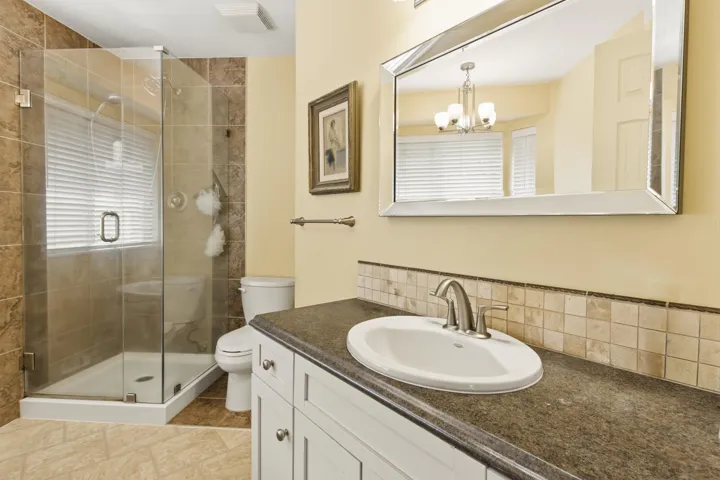 Bathroom featuring a glass-enclosed shower, a vanity with an undermount sink, a stone-look countertop, and a tiled backsplash