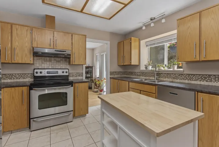 Kitchen featuring wood cabinetry, stainless steel appliances, tiled backsplash, and a central island with a wood-finish countertop