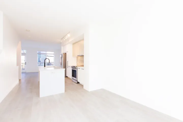 Kitchen with light countertops, a kitchen island with sink, appliances with stainless steel finishes, rail lighting, and light wood finished floors
