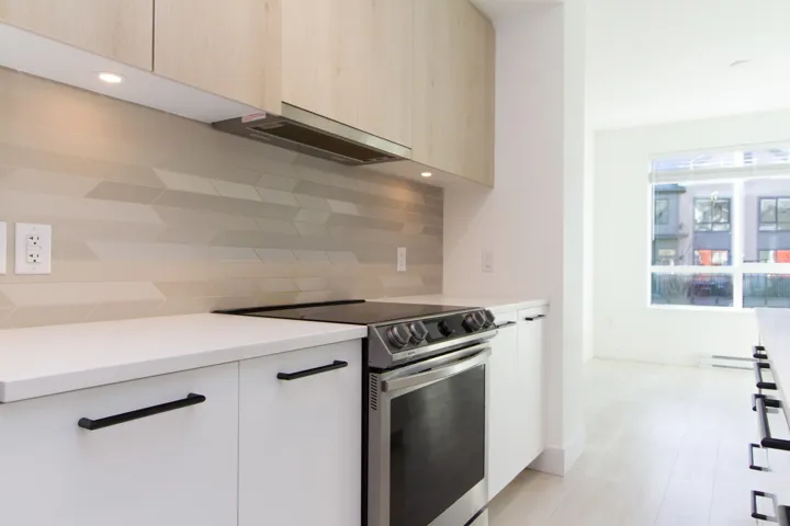 Kitchen with stainless steel range with electric stovetop, modern cabinets, under cabinet range hood, backsplash, and light wood-style floors