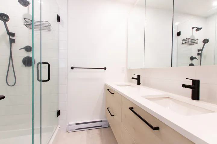 Bathroom featuring double vanity, a baseboard heating unit, and a stall shower