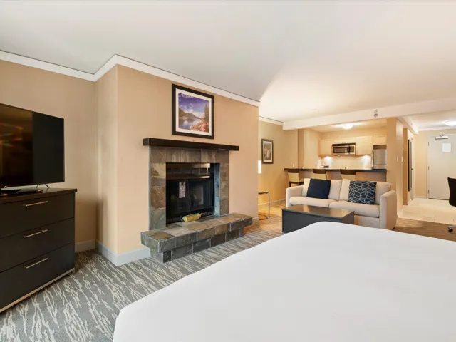 Bedroom with a tiled fireplace, baseboards, light colored carpet, stainless steel refrigerator, and ornamental molding