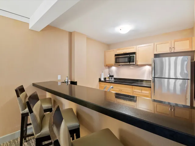 Kitchen with a kitchen breakfast bar, dark countertops, light brown cabinets, baseboards, and appliances with stainless steel finishes