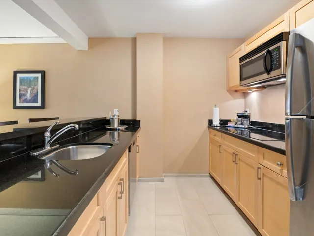 Kitchen with light brown cabinetry, dark countertops, light tile patterned floors, a sink, and appliances with stainless steel finishes