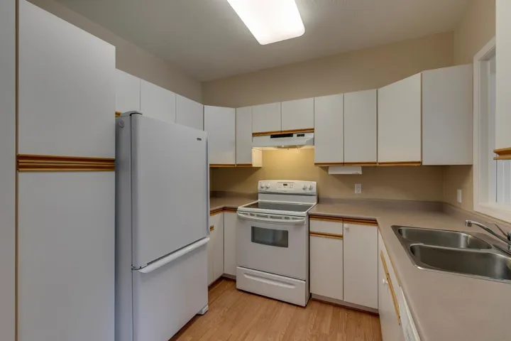 Kitchen with white cabinets, white appliances, light wood-type flooring, light countertops, and under cabinet range hood