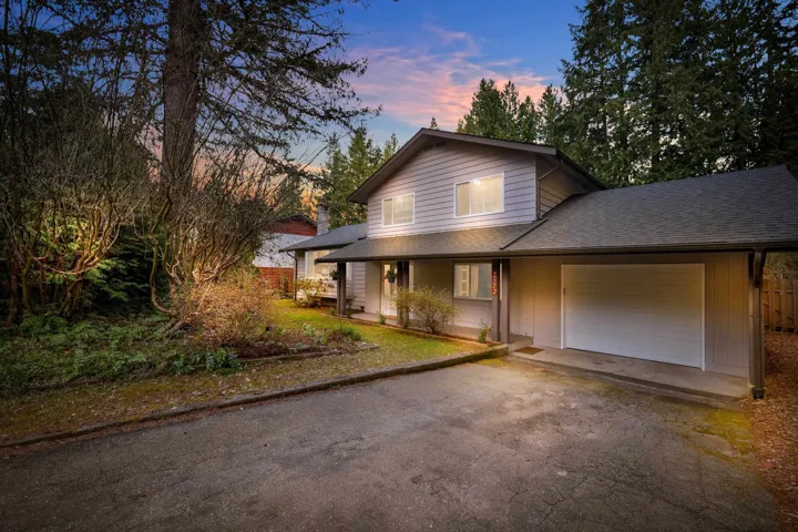 View of front facade with roof with shingles, an attached garage, asphalt driveway, and a porch