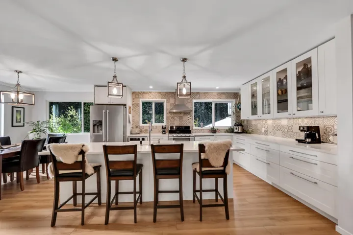 Kitchen featuring glass fronted cabinets, a center island with sink, stainless steel appliances, a kitchen bar, and decorative light fixtures