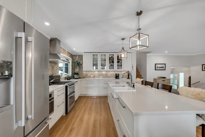 Kitchen with stainless steel appliances, glass fronted cabinets, white cabinets, light wood-type flooring, and tasteful backsplash