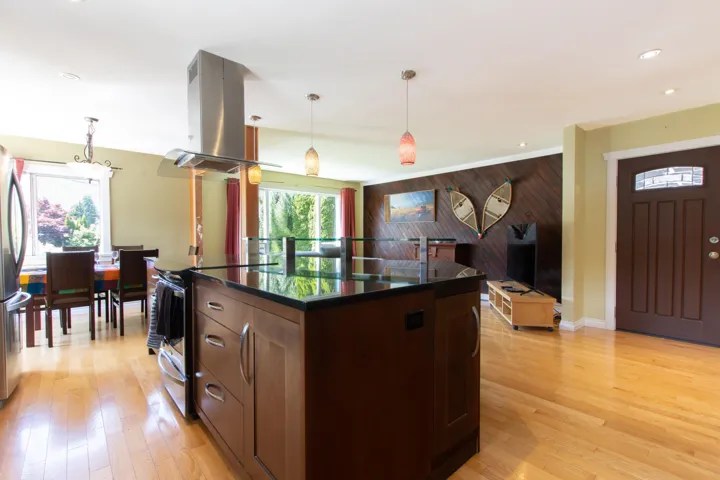 Kitchen with island range hood, stainless steel appliances, dark countertops, wood walls, and pendant lighting