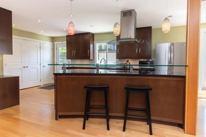 Kitchen with island range hood, freestanding refrigerator, dark countertops, light wood finished floors, and a kitchen breakfast bar
