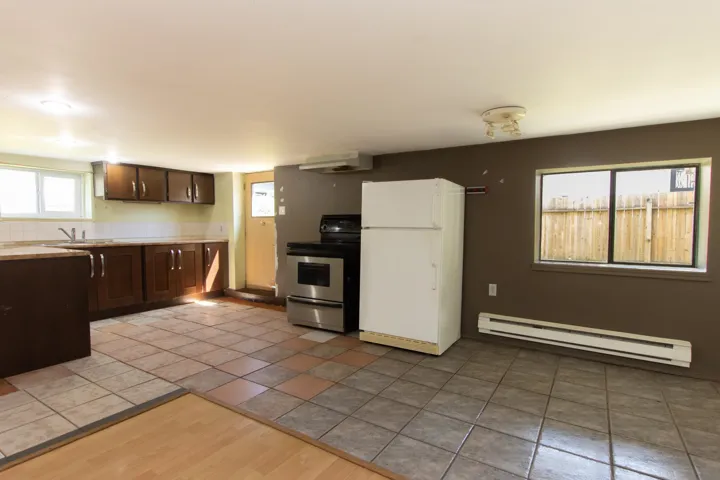 Kitchen featuring freestanding refrigerator, a baseboard radiator, stainless steel electric stove, exhaust hood, and light countertops