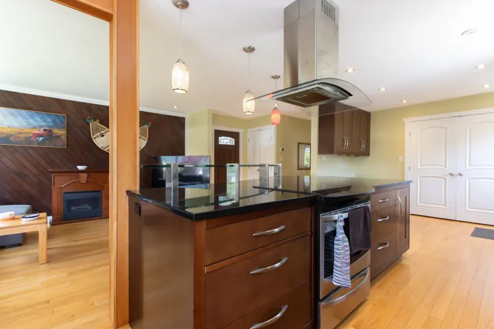 Kitchen with island exhaust hood, dark countertops, stainless steel range with electric stovetop, wooden walls, and light wood-type flooring