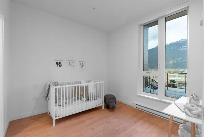 Bedroom with a baseboard heating unit, multiple windows, a crib, and light wood-style floors