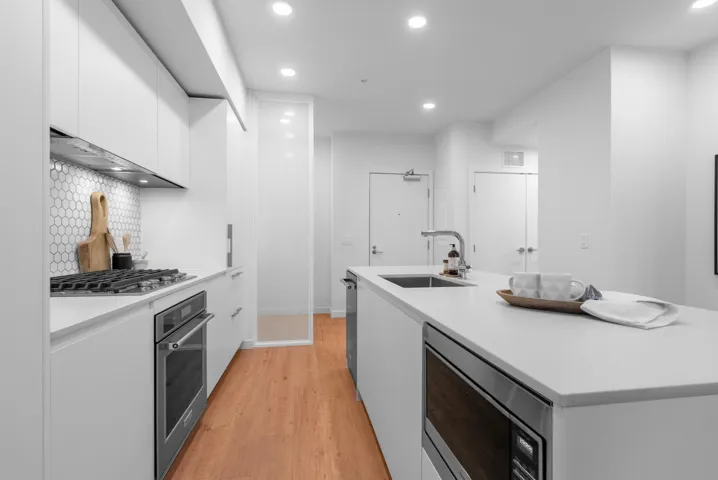 Kitchen with modern cabinets, white cabinetry, stainless steel appliances, recessed lighting, and an island with sink