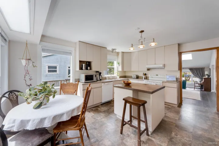 Kitchen with white appliances, under cabinet range hood, a kitchen island, a sink, and hanging light fixtures