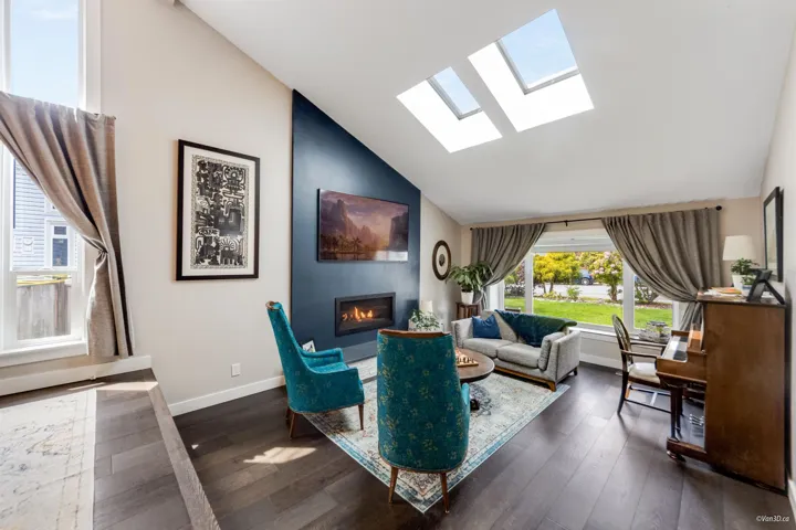 Living area featuring a skylight, lofted ceiling, a glass covered fireplace, baseboards, and dark wood-style flooring