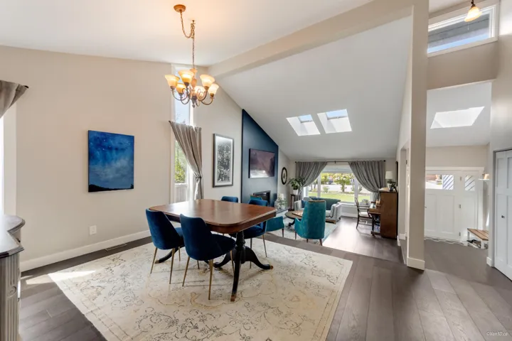 Dining space with a skylight, hardwood / wood-style floors, vaulted ceiling, a chandelier, and baseboards