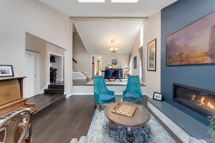 Living area featuring stairway, dark wood-style flooring, a chandelier, a glass covered fireplace, and baseboards