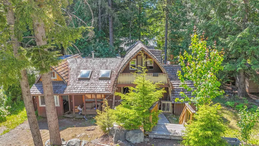 Wood-shingled exterior set among mature trees, featuring a prominent A-frame structure with a second-story balcony