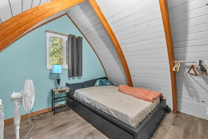 Vaulted ceiling room featuring natural wood beams and wood-finish flooring
