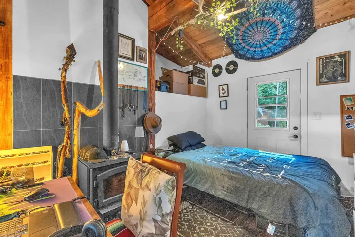 Interior space featuring a wood-burning stove with a dark tile backsplash, exposed wood ceiling beams, and white walls