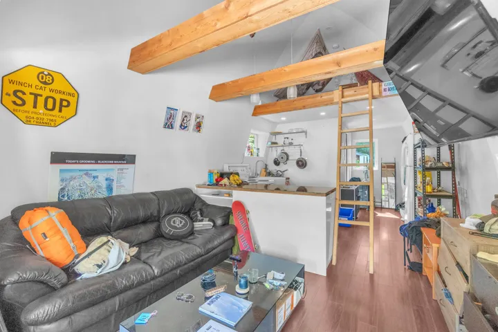Open-concept living space featuring vaulted ceilings with exposed wood beams, wood-finish flooring, a kitchen bar counter, and a built-in loft with ladder access