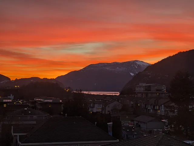 Expansive mountain and water scenery under a vibrant orange and red sky