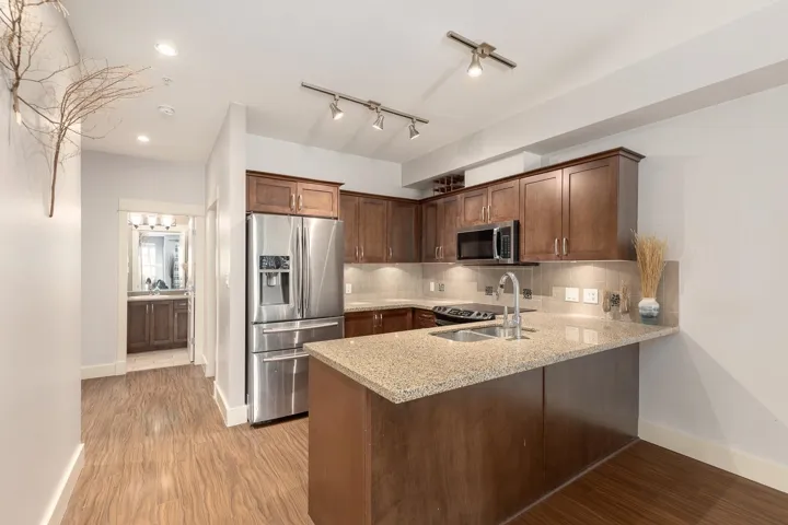 Kitchen featuring wood-finish flooring, stainless steel appliances, granite countertops, wood cabinetry, and recessed lighting
