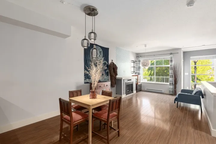 Open-concept living area featuring wood-finish flooring, a contemporary fireplace with a light-colored mantel, and large windows providing ample natural light