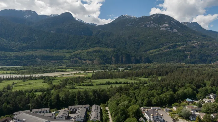 Expansive mountain landscape with forested slopes, a winding river, and verdant fields