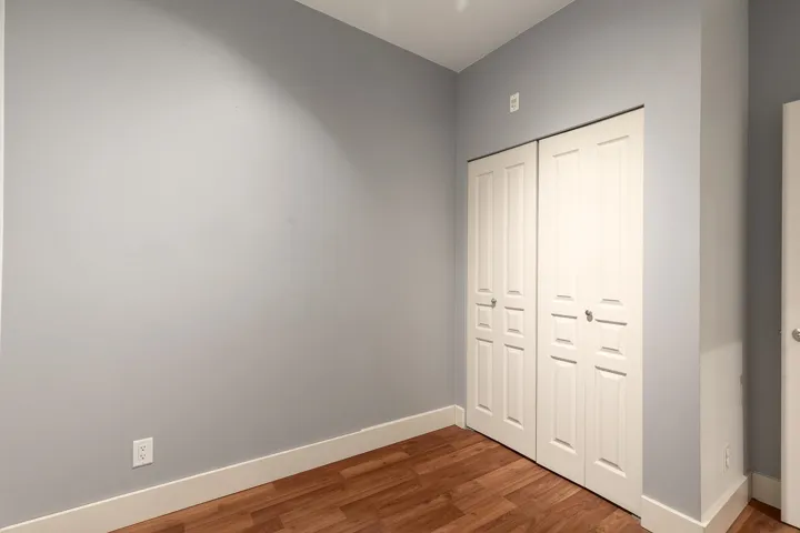 Room featuring a bi-fold closet with panel doors, wood-finish flooring, light gray wall paint, and white baseboards