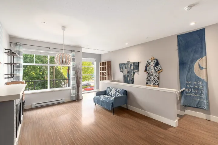 Open-concept living area featuring wood-finish flooring, a large picture window, and a built-in kitchen island with a light-toned countertop