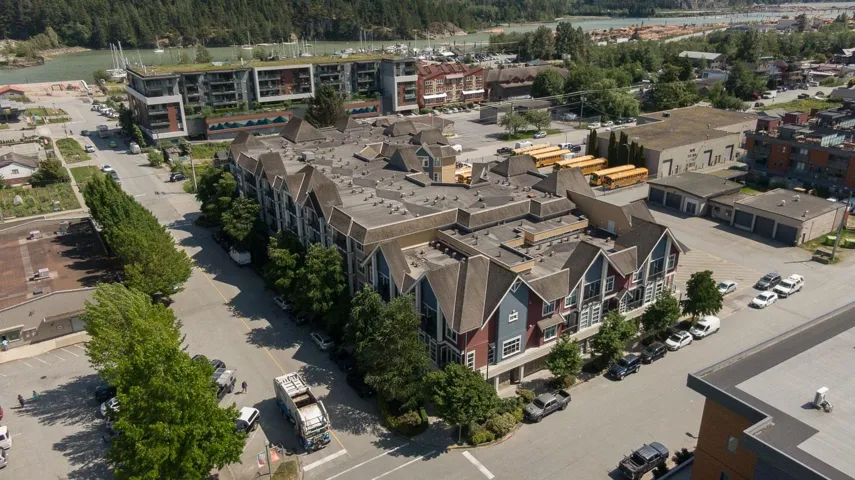Multi-story residential building featuring gabled rooflines, varied siding in red and blue tones, and ample street parking