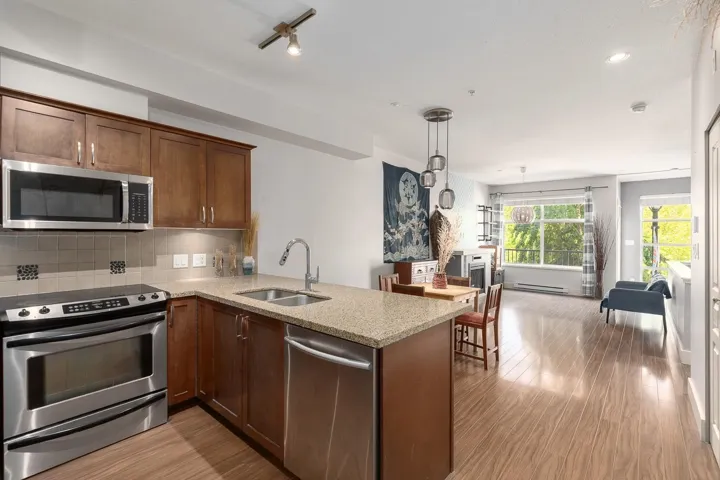 Open-concept kitchen featuring stainless steel appliances, wood cabinetry, and a granite-style countertop with an undermount double sink