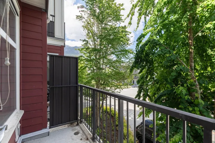Balcony with black metal railings and a privacy screen, featuring a red siding exterior and surrounding mature trees