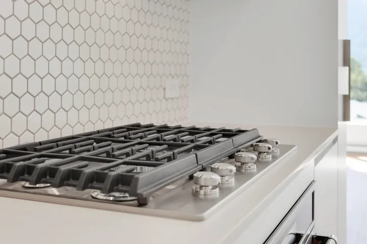 Kitchen view of stainless steel gas stovetop, white cabinetry, and backsplash