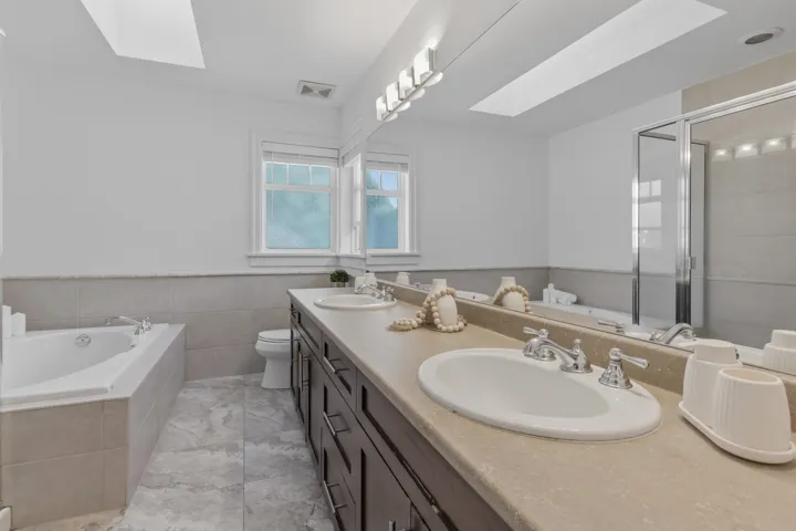 Full bathroom featuring a skylight, a bath, double vanity, a shower stall, and a wainscoted wall