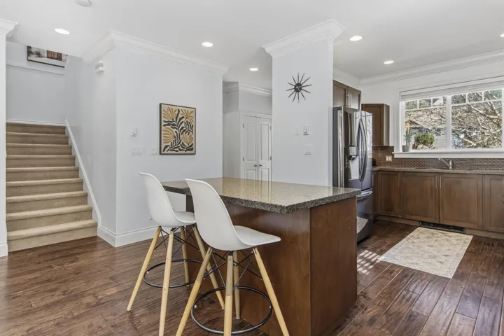 Kitchen featuring stainless steel fridge, ornamental molding, backsplash, dark wood-style floors, and a breakfast bar area