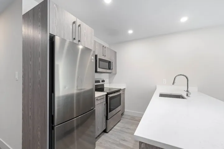 Kitchen with stainless steel appliances, a sink, a peninsula, light wood-type flooring, and light countertops