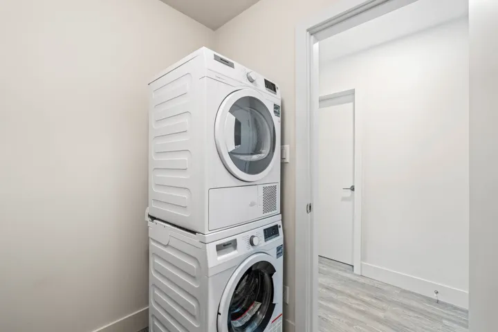 Laundry area featuring stacked washer / dryer, light wood-style flooring, and baseboards