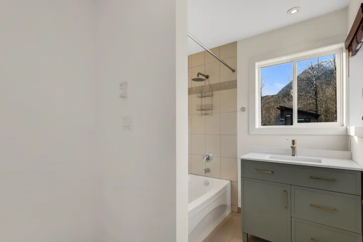 Bathroom featuring a white bathtub, tiled shower surround, recessed lighting, and a window