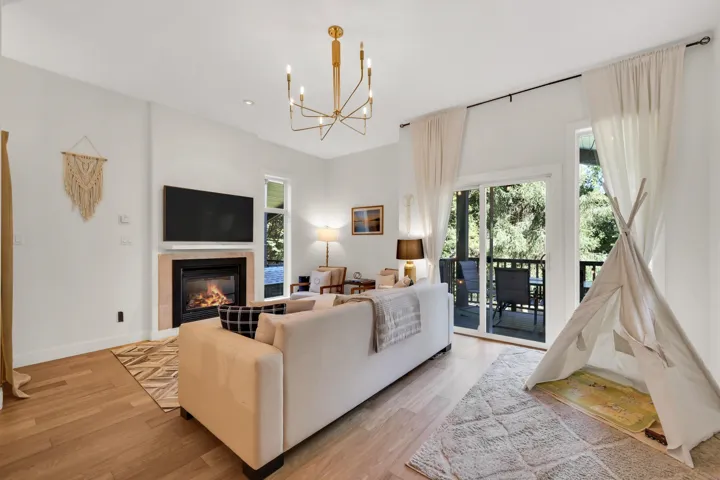 Spacious living area featuring light wood-finish flooring, a contemporary fireplace with a light-toned surround, a gold-toned chandelier, and a large sliding glass door with balcony access