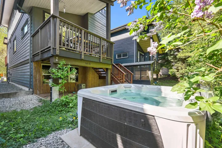 Outdoor spa with surrounding gravel and greenery, set below a wood-decked patio with dark railings